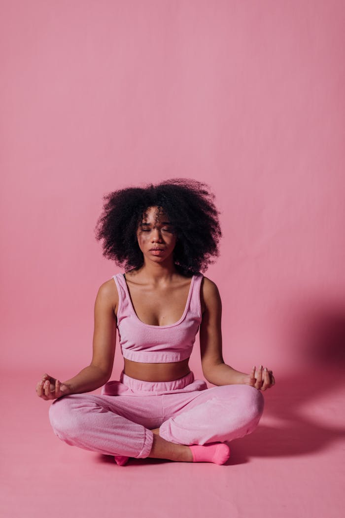 Offerings A woman meditating in yoga pose against a pink backdrop, embracing tranquility.